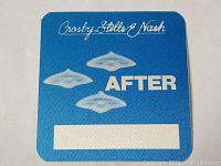 Blue laminated concert tour pass with white cursive 'Crosby Stills Nash' text, three white flying saucer images, and 'AFTER' text.