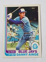 Front photo of 1982 O-Pee-Chee baseball card featuring Danny Ainge batting for the Toronto Blue Jays, with autograph and 'Voluntarily Retired' stamp.
