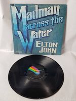 Photo of the vinyl record disc partially placed in front of the album cover showing the black vinyl and MCA label.