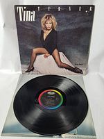 Full view of vinyl record with album cover behind it showing the partial label and record surface condition.
