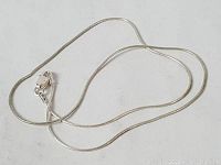 Sterling silver braided chain necklace with lobster clasp loosely coiled on a white surface.