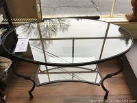 Oval glass top coffee table showing the entire top surface and iron frame structure underneath.