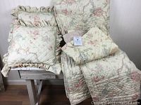 Full view of the cotton quilt spread and two matching pillow shams with ruffled edges plus two decorative pillows arranged on a bench.