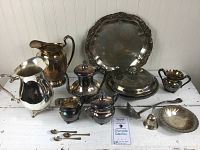 Full view of all 16 silverplated items arranged on white surface including trays, pots, pitchers, and serving pieces