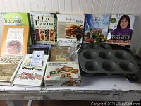 Wide shot showing all cookbooks lined up alongside bakeware and storage containers on a wooden surface.