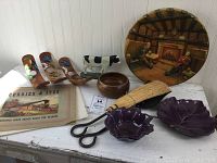 Full display of all items on a table: decorative plate, butterfly wooden holders, cow figurine, wooden bowl, metal scissors, purple ceramic leaf bowls, vintage metal sign, woven brush.