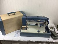 Photo of vintage White sewing machine in blue and cream, inside the hard carrying case with lid removed, includes power cord and foot pedal.