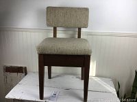 Front view of vintage wooden sewing bench with beige textured upholstery on seat and backrest.