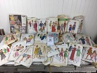 Wide view of a large assortment of vintage women's and girls' sewing pattern envelopes, various sizes, different brands, spread on a table.