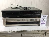 Two stacked components, top is Technics CD player, bottom is Harman Kardon VCD 4000 VHS VCR with control panel.