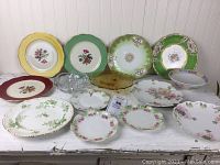 Front view of assortment of vintage European china including various plates and glass dishes showing floral and gold designs.