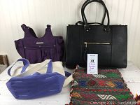 Front view of the lot showing a black leather look handbag, purple Ariat bag, small cream and purple LL Bean tote, and a colorful woven bag.