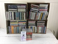 Four boxes stacked two on bottom two on top, containing hundreds of CDs in jewel cases with visible titles and colored spines showing different types of music and collections.