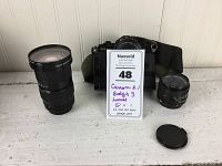 Photo showing all items: Canon A-1 camera with power winder, the three lenses, and a lens cap on white surface.