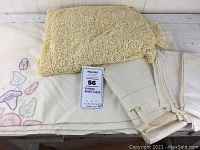 Overview of the full set of vintage table linens including crocheted tablecloth on top, damask tablecloth underneath with colorful appliques, and folded damask napkins on the right.