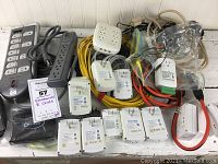 Wide view showing a mix of several power strips, extension cords, Smartlabs units, and plugs arranged on a white surface.