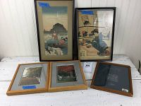 Photo showing two Asian prints in frames and four other frames/photos, laid out on white surface against wood paneling