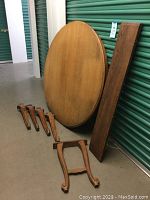 Disassembled round oak table with five pieces: tabletop, two leaves, and four legs.