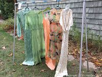 Full rack view showing five dresses (aqua satin, green beaded, peach slip, printed chiffon, ivory cowl-neck) hanging outdoors