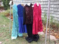 Four vintage garments on hangers; three dresses and one outfit with pleated pants, displayed outdoors on a metal rack.