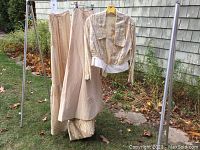 Full view of two skirts and dragon embroidered jacket hanging on rack outdoors, showcasing overall garments and colors