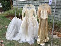 Full view of two wedding gowns hanging on a metal frame outdoors with white full tulle petticoat hanging separately
