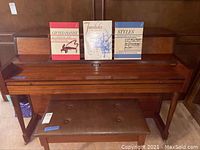Front view of Heritage console piano with bench and three sheet music books displayed on rack