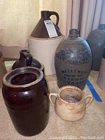 Five pottery crocks of various sizes and colors arranged together on carpet, showing overall condition and detail of each.