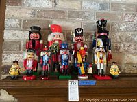 Eleven nutcrackers including nine wood and two ceramic candle-shaped nutcrackers arranged on a shelf with brick background.