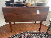 Front view of antique wooden drop leaf table closed, showing rectangular top and slender legs on casters.