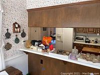 Long shot showing countertop with multiple glassware items, decanter, cheese dishes, and glass tumblers along with some ceramic and metal items on the kitchen counter area.