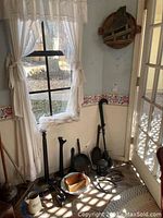 Corner showing heavy cast metal weights, vintage lantern, ice tongs, and other metal tools on floor near window and door.