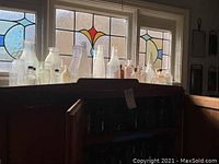 Glass jars and bottles displayed in front of a stained glass window, showing varied shapes and sizes in clear and amber glass.