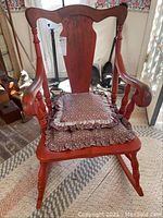 Front view of vintage red painted rocking chair with cushions showing seat and back cushions with floral pattern