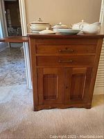 Front view of antique wooden cabinet with items on top and extended pull-out side tray