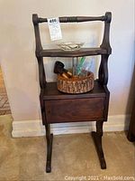 Front view of antique wooden humidor stand with decorative sides, shows glass dish on top shelf and wooden bowl with nutcracker on lower shelf, cabinet closed.