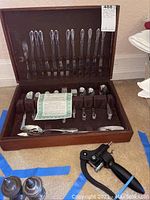 Full view of flatware set in open wooden case showing knives, forks, spoons, serving utensils, and wine opener.
