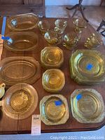 Overview of multiple yellow Depression glass serving pieces, plates, bowls, and cups arranged on a wooden table.