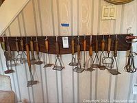 View of entire wood rack with hanging vintage potato mashers and egg beaters