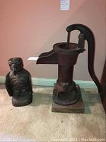 Overview of both items: Native Alaskan bird sculpture and cast iron pump side by side on carpet.