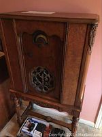 Full frontal view of wooden floor radio on turned legs with ornate grille and control knobs