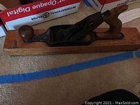 Long wood-bodied hand plane with metal blade, showing the top and side profile with wooden front round knob and rear handle.