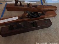 Three large woodworking planes arranged on floor, two wooden-bodied planes and one metal-bodied plane with wooden handles.