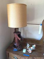 Full view of water pump lamp with beige fabric shade alongside three ceramic clown figurines on wooden surface.