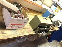 Photo of bench grinder, electrical cords, hardware box, and metal tool organizer on workbench.