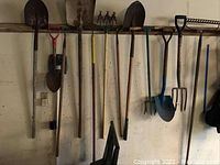 Wide view of all hanging yard tools including shovels, pitchfork, rake, and tiller.