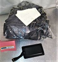 Lot of 35 black leather luggage tags wrapped in plastic with folded note on top showing lot info