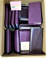 Box lot of 25 leather-bound weekly planners arranged inside a cardboard box, showing brown and burgundy covers stacked and aligned.
