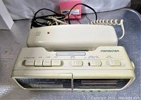 Front and top view of beige Soundesign combo device showing clock radio, cassette player, buttons, and attached telephone handset with cords.