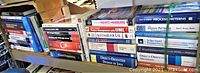 Wide view of computer programming books stacked on shelves showing partial titles and book spines.